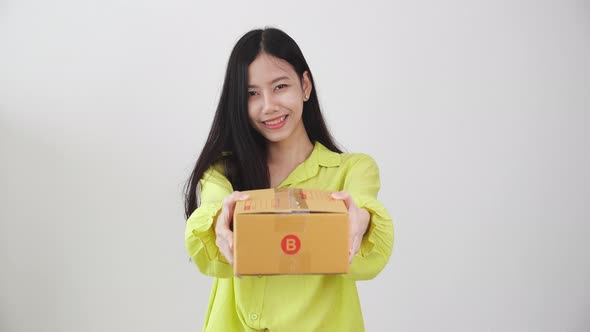 Young asian woman smiling and holding cardboard box at home, happy female carrying parcel box giving alt