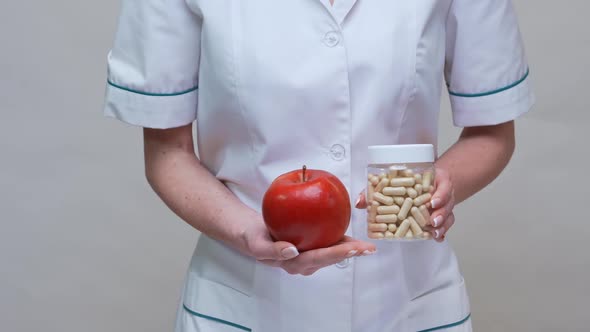 Nutritionist Doctor Healthy Lifestyle Concept - Holding Organic Red Apple and Jar of Vitamin Pills alt