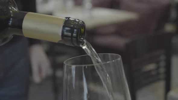 Closeup and Front View with Copy Space of Serving White Wine Being Poured From a Bottle Into Clear