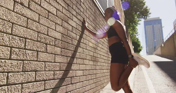 African american woman exercising outdoors leaning of wall and stretching in the city alt