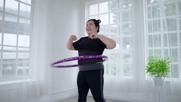 Fat Asian woman playing hula hoop to lose weight cheerfully in her room