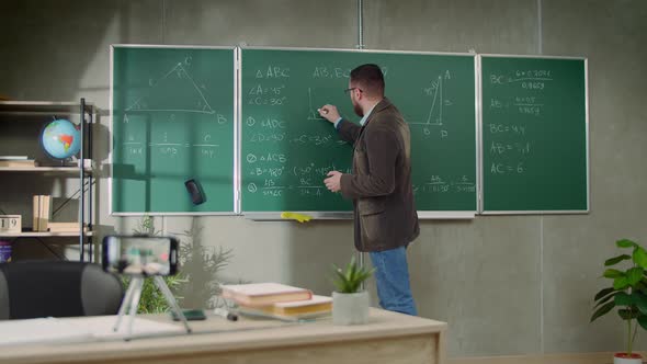 Young Man Teacher Shoots Video Lesson on Geometry on Smartphone in the Classroom During Quarantine alt