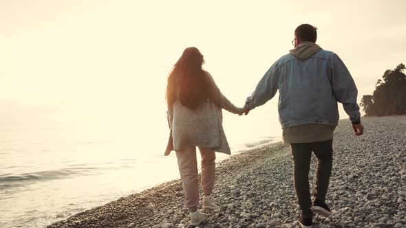 Loving Couple Is Walking Over Pebble Beach Near Sea in Sunset Time alt