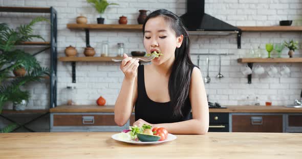 Asian Woman Sitting at Table Looking Sad and Bored with Diet Not Wanting to Eat Salad alt