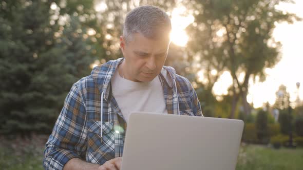 A Focused Male Freelance Programmer Works on a Laptop in a City Park