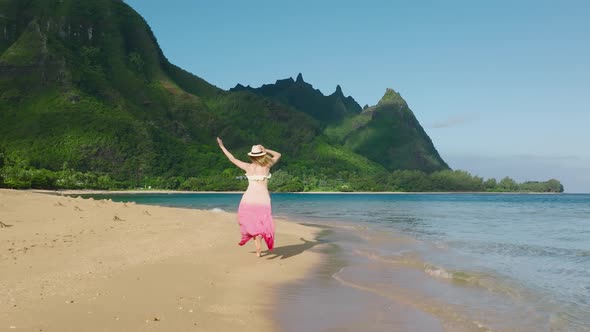 Slow Motion Young Woman in Colorful Dress Running By Beach to Mountain Peaks alt