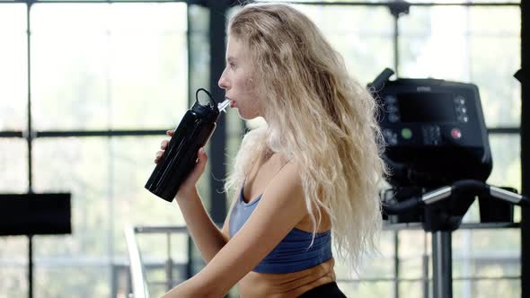 Athletic Woman Drinks Water From a Bottle and Rests After Training in the Gym alt