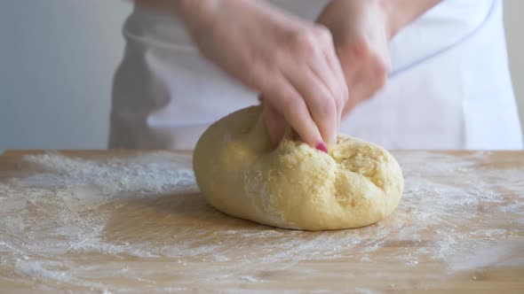 Woman kneading pastry dough on floured baking board
