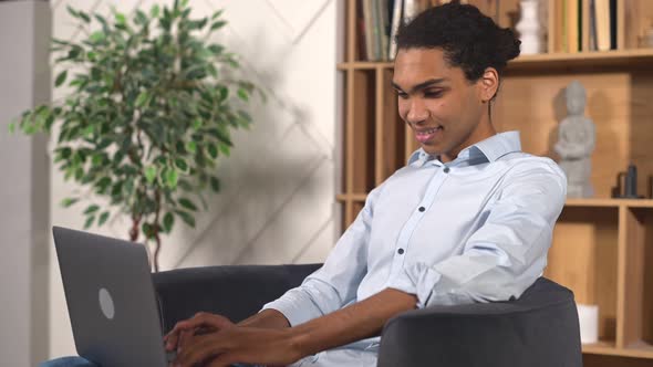 Optimistic Ethnic Man in Casual Wear Using Laptop While Sitting on the Couch