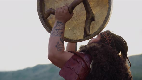 Obese Man Plays Shamanic Tambourine Praying Against Hills alt