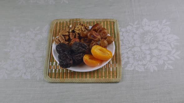 Apricots Prunes Dates Walnuts on a White Saucer Standing on a Bamboo Napkin alt