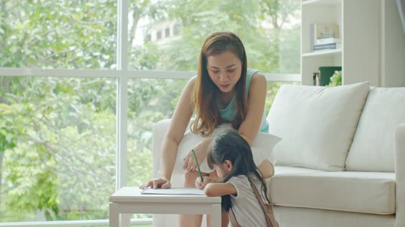 Pretty mother laughing while looking her daughter drawing on paper