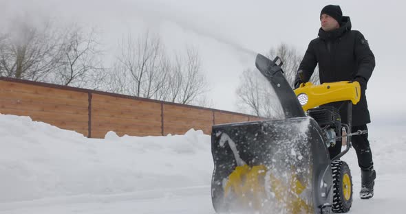 Man Cleans Snow With Snowplough at Wooden House Backyard in Winter alt