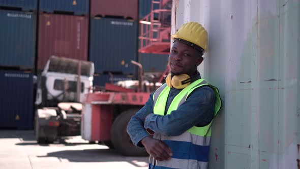 Smiling man in hard hat standing with crossed arms at container cargo site
