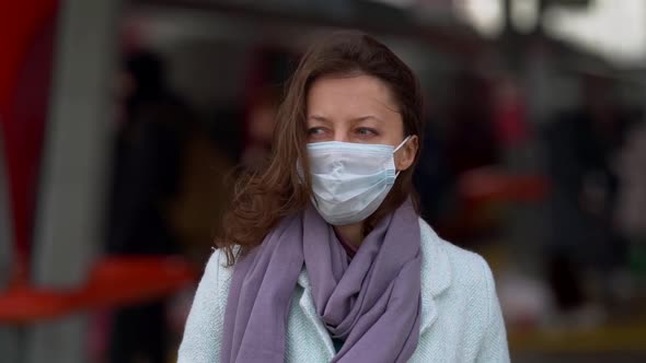 Adult Woman with Facial Mask Is Standing on Train Station at Windy Autumn Day alt