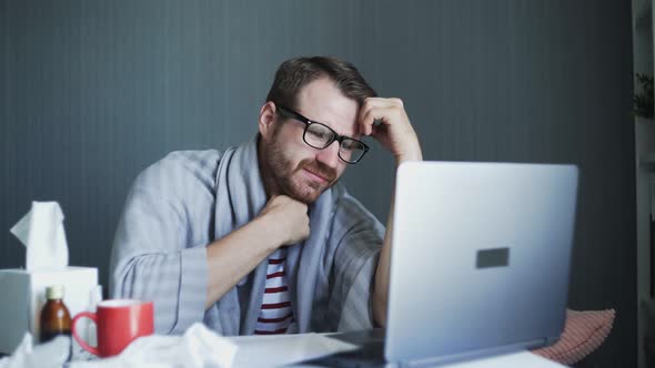 Young Freelancer Working From Home During Illness. Sick Business Man Working with Laptop Computer alt