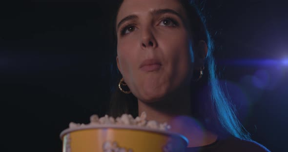 Young woman watching a movie at the cinema and eating popcorn