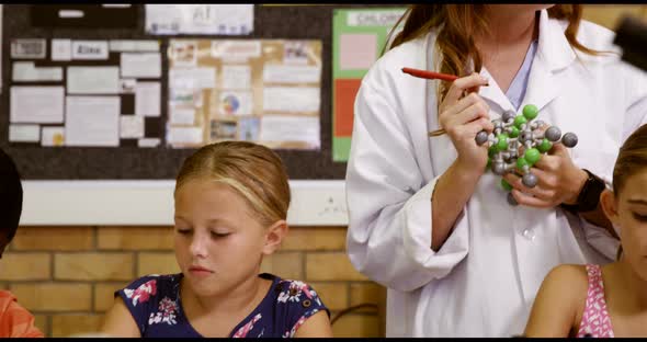 Teacher assisting school kids with molecule model in laboratory alt