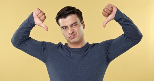 Young man feeling disappointed and making thumbs down gesture in yellow isolated studio background