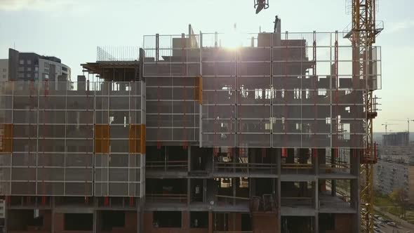 Raising the Camera Up Along a Building Under Construction with Empty Floor Spans and Workers on the