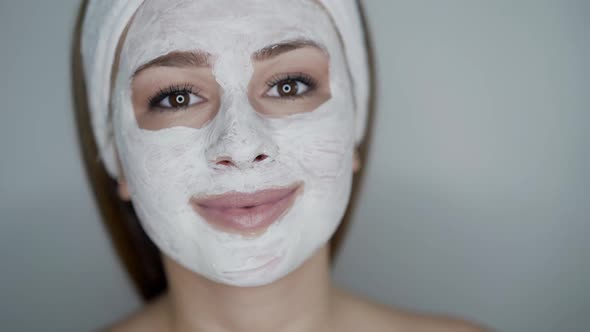 Cute Girl with Cosmetic Mask on Face Looks with Smile Into Camera on Background alt