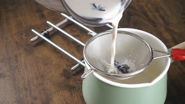 Milk mixture being poured to drain in mesh stainless steel colander into the pot for eggnog cooking