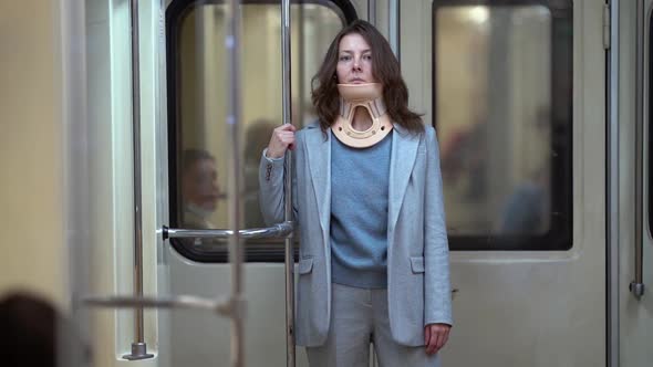 Adult Injured Woman with Cervical Collar Inside Subway Train, Standing and Holding Handrail alt