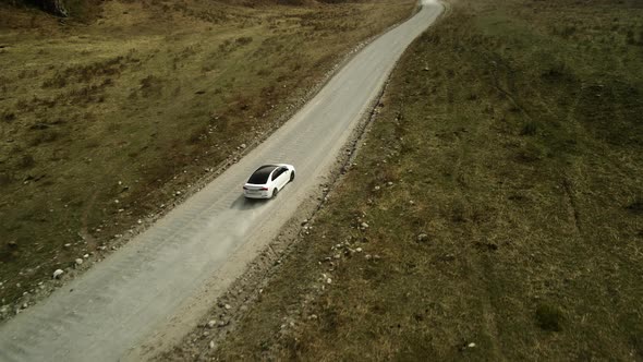 A White Sedan Moves Offroad in a Mountainous Area alt