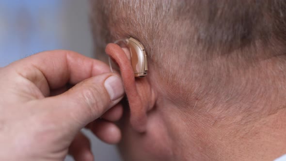 Man Wears Hearing Aid with Fingers Near Ear