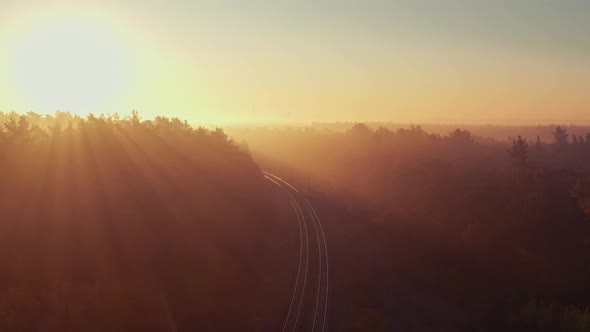Railway road in the foggy forest at sunrise. Aerial view.