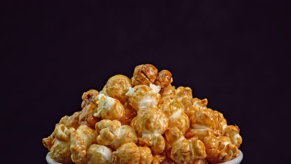 Coffee taste popcorns rotating into the bowl on black background close up. Caramel popcorn. Health alt