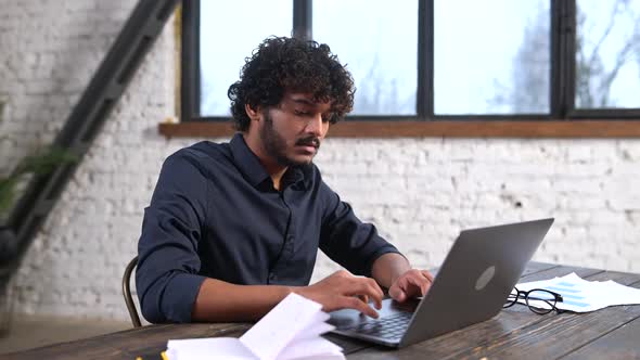 Confident Concentrated Indian Freelancer Guy Working on Laptop at Home Office alt