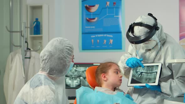 Dentist in Protective Equipment Showing on Tablet Dental Xray of Child alt