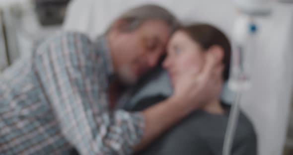 Man Visiting Sick Wife in Hospital Lying in Bed Together and Talking alt