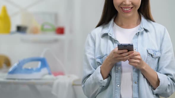 Smiling Housewife Chatting on Smartphone, Leaving Iron on Board, Risk of Flame alt