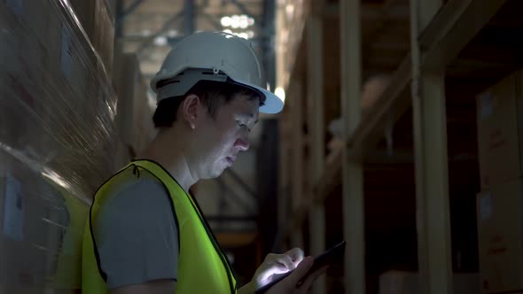 Young Warehouse Worker Man with Safety Hard Hat Checking Order Details with Tablet at Inventory Room alt