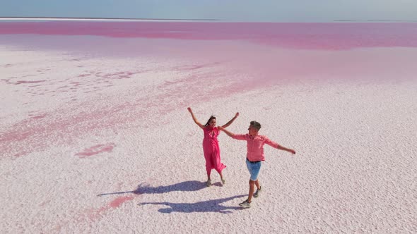 Aerial Drone Footage of Happy Joyful Couple Having Fun and Walking on Bright Colorful Pink Water of alt