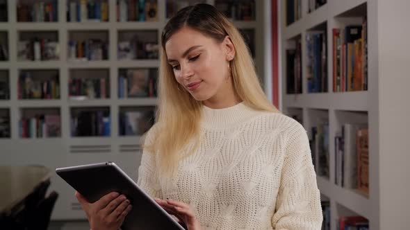 Portrait of a Young Female Student in the Library with a Tablet alt