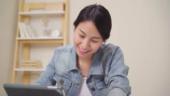 Young asian woman working using tablet checking social media while relax on desk . alt