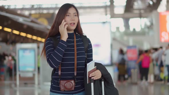 Young female traveler talking with smartphone to someone at airport alt