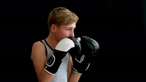 A Teenage Athlete Stands on a Dark Background. His Hands Are in Black and White Gloves alt