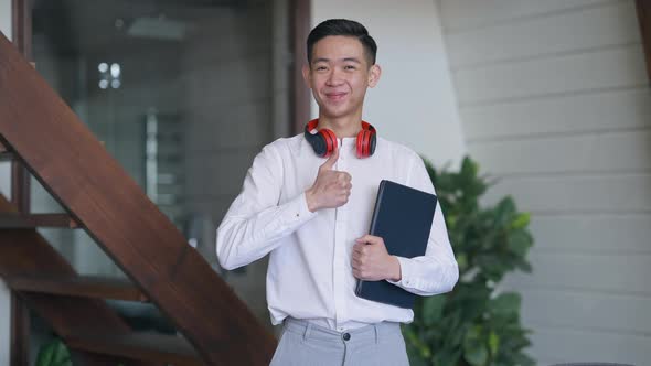 Middle Shot of Happy Smiling Chinese Man Showing Thumb Up Looking at Camera Standing in Living Room alt