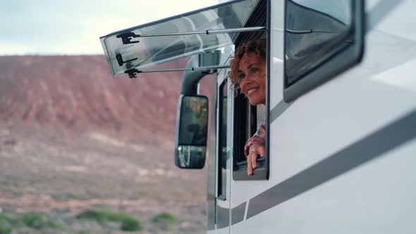 Excited young adult woman admire beautiful outdoors from the camper van window inside. alt