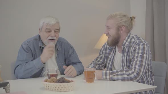 Positive Elderly Caucasian Man Taking Ear of Adult Son and Waving Finger. Cheerful Male Retiree alt