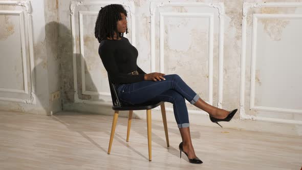 Exciting Black Lady in Blue Jeans Sits on Brown Wooden Chair alt