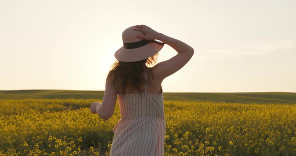 A Smiling Girl Is Running Across the Field and Holding on Her Hat alt