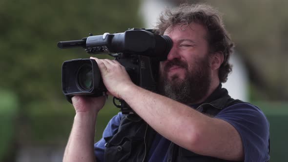 Bearded television cameraman filming outdoors.