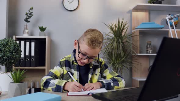 10-Aged Modern Boy in Glasses which Writing Down the Notes into Notebook from Computer alt