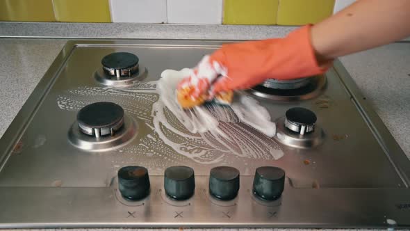 Housewife in Gloves Washes the Gas Stove in Kitchen with a Washcloth and Foam alt