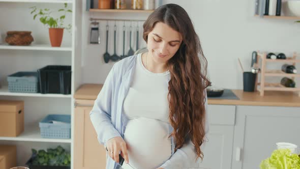 Happy Pregnant Woman Enjoying Preparing a Salad Cutting Organic Vegetables alt